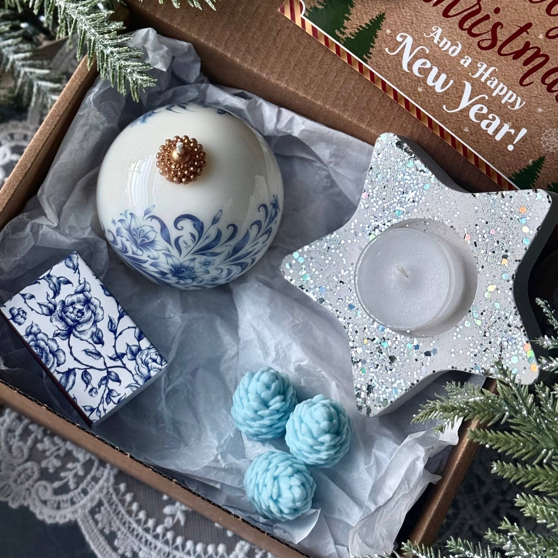 Decorative items including a white ornament with blue patterns, teal spherical decorations, and a star-shaped candle holder in a Christmas-themed box.