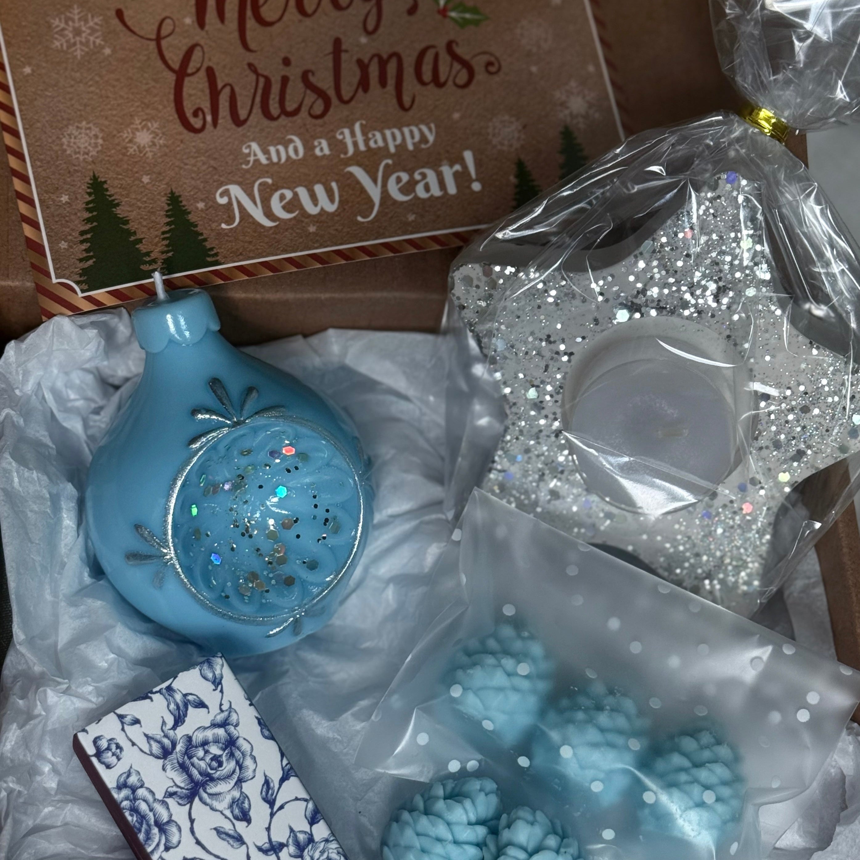 Box of Christmas decorations including a blue ornament candle, star-shaped candle holder, and pine cone-shaped items.