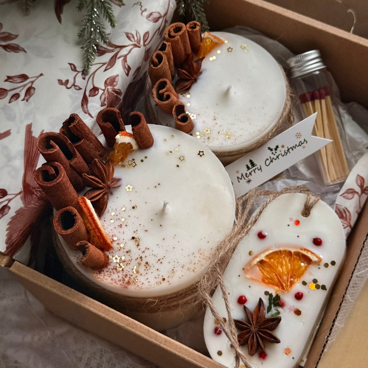 Decorative candles with cinnamon sticks and orange slices in a gift box.