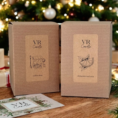 Two VR Candle boxes with labels on a wooden surface with a Christmas tree in the background.