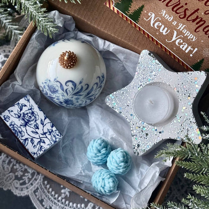 Decorative items including a white ornament with blue patterns, teal spherical decorations, and a star-shaped candle holder in a Christmas-themed box.