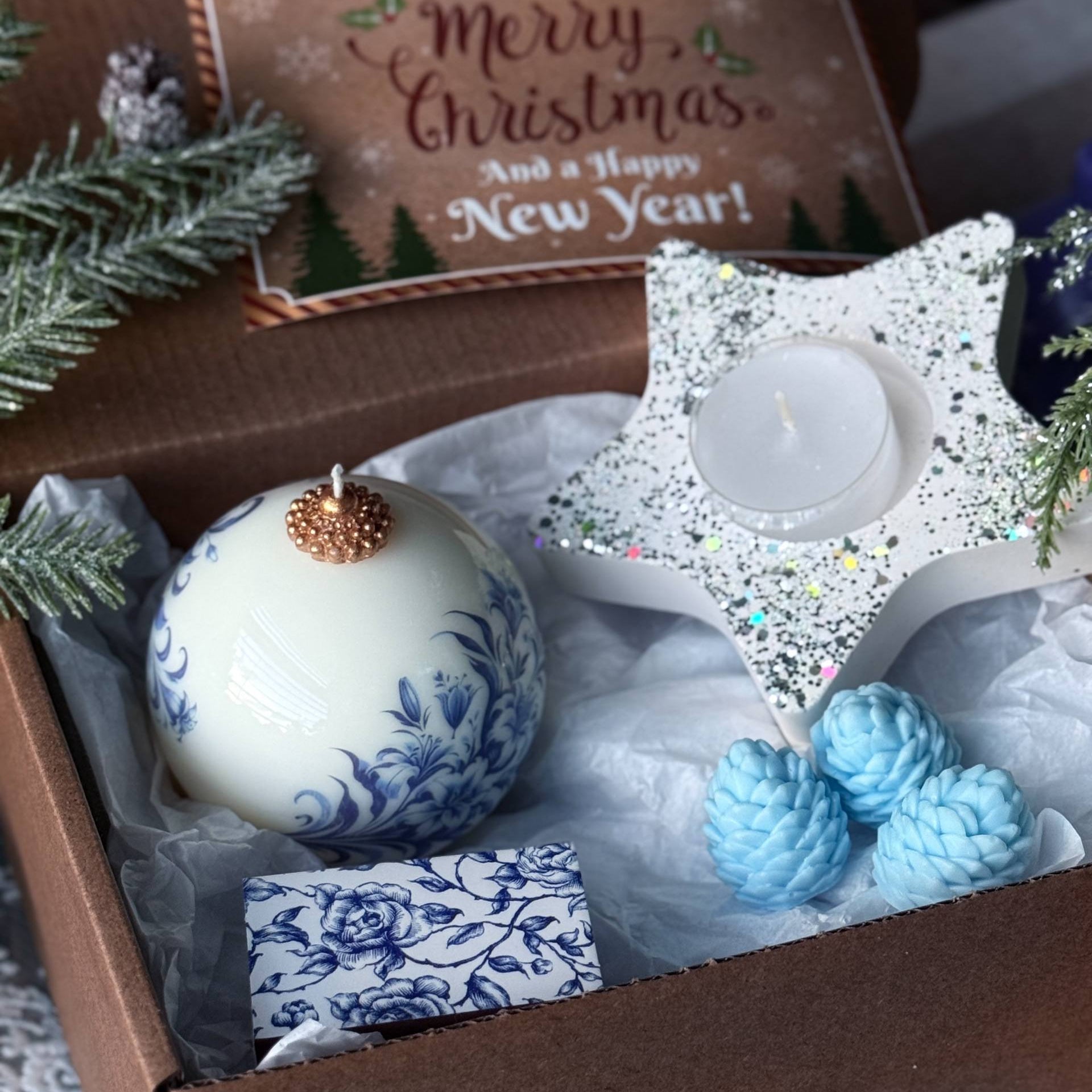 Decorative Christmas items including a white ornament with gold top, blue pinecones, and a star-shaped candle in a box.