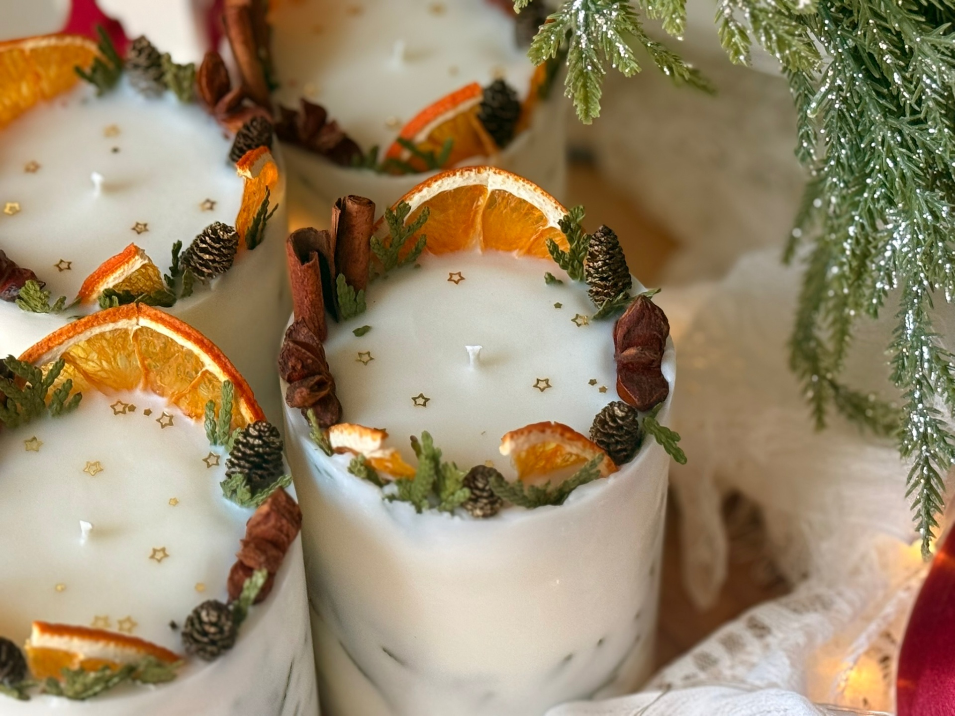 Close-up of a handmade Christmas decorative candle with dried orange slice, cinnamon, star anise, pine cones, and gold star accents